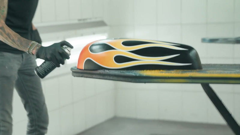 Painter holding a spray can beside a motorcycle tank with finished orange flames